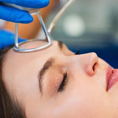 Close-up of a patient lying down, wearing protective eyewear, as a clinician in blue gloves handles a medical tube near the face during a procedure.